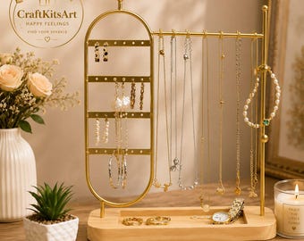 May include: A gold-toned metal jewelry organizer stand with a light wood base. The stand features a vertical oval frame with holes for earrings and a horizontal bar for hanging necklaces. Several necklaces, a pearl bracelet, and a watch are displayed.