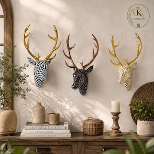 May include: Three wall-mounted deer head sculptures featuring checkered patterns and metallic antlers. The left deer is black and white with gold antlers, the centre is dark grey with bronze antlers, and the right is white and gold with gold antlers.
