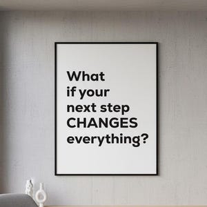 以下が含まれることがあります： 「What if your next step CHANGES everything?」のテキストが入った額縁がコンクリートの壁に掛けられています。灰色のアームチェア、小さなガラスのテーブル、ベージュのラグが壁の前にあります。テーブルには小さな植物が置かれています。