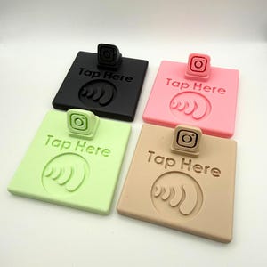 May include: Four square NFC stands in black, pink, light green, and tan. Each stand features a small Instagram logo icon at the top, the text "Tap Here" in the center, and a circular contactless signal symbol embossed at the bottom.