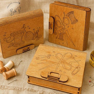 May include: Wooden sewing boxes with etched designs of spools, scissors, and needles. The boxes are various shapes and sizes, with a natural wood finish and a clasp closure. The boxes are displayed on a neutral-coloured fabric.