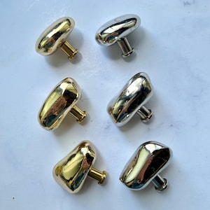 May include: A set of six cabinet knobs with irregular, organic shapes. Three knobs feature a polished gold finish, while the other three have a reflective silver finish. Each knob includes a short, cylindrical stem and a flat circular base.