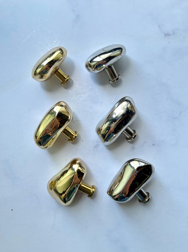 May include: A set of six cabinet knobs with irregular, organic shapes. Three knobs feature a polished gold finish, while the other three have a reflective silver finish. Each knob includes a short, cylindrical stem and a flat circular base.