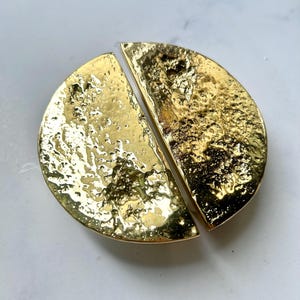 May include: Two gold-colored, semi-circular cabinet pulls with a textured surface. The hardware is arranged to form a circle, with a gap between the two pieces. The pulls have a shiny, metallic finish.