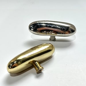 May include: Two oval-shaped cabinet knobs. One is silver-toned, the other is gold-toned. Both knobs have a smooth, polished finish and are mounted on short stems. The knobs are likely for furniture or decorative use.