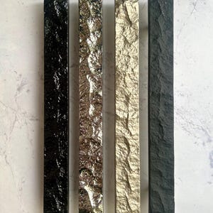 May include: Four rectangular decorative pieces with textured surfaces. The pieces are in black, silver, gold, and dark grey. The surfaces have a rough, stone-like appearance, adding a unique texture to the design.