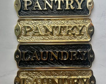 Op de afbeelding: Vier rechthoekige metalen borden met de woorden "PANTRY" en "LAUNDRY" in reliëf. Twee borden zijn zwart met gouden letters en twee zijn goudkleurig met zwarte letters. Elk bord heeft een decoratieve rand en gaten.