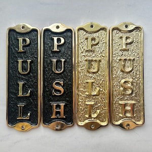 May include: Four rectangular brass door signs. Two signs read "PULL" and two read "PUSH". The "PULL" signs have a black background, while the "PUSH" signs have a gold background. All signs have gold lettering.