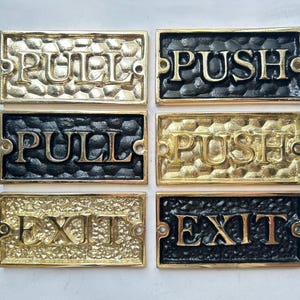 May include: Rectangular brass door signs with the words "PULL", "PUSH", and "EXIT" in raised lettering. The signs are in gold and black, with a textured background and holes for mounting.