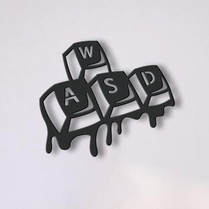 Könnte beinhalten: Schwarze Metall-Wandkunst mit den Buchstaben WASD einer Computertastatur, mit einem tropfenden Farbeffekt. Das Kunstwerk ist an einer weißen Wand über einem weißen Sofa mit dekorativen Kissen und einem runden Couchtisch angebracht.