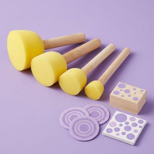 Può includere: Quattro applicatori di vernice in schiuma gialla con manici in legno sono disposti su una superficie viola. Ci sono anche tre cerchi di feltro viola e due piccoli blocchi di legno con motivi a pois viola. Per l'artigianato.