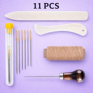 May include: An 11-piece leathercraft tool kit on a purple background. The kit includes a bone folder, needles, a thread spool, a stitching awl, and other tools. The tools are in various colors, including beige, gold, and brown.