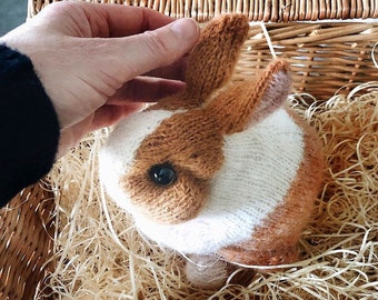 May include: A knitted brown and white bunny rabbit toy in a wicker basket with shredded paper.