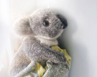 May include: A gray knitted koala plush toy wearing a floral print dress with yellow accents.