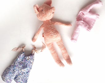 Peut inclure: Une poupée en tricot rose en forme de cochon avec un pull en tricot rose et une robe à imprimé floral avec des rubans assortis.