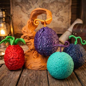 Puede incluir: Una colección de esculturas de frutas coloridas y texturizadas, que incluyen una piña roja, una fruta morada, turquesa y azul oscuro. Las frutas tienen patrones arremolinados y se exhiben sobre una superficie de madera con un mapa y un cofre del tesoro en el fondo.