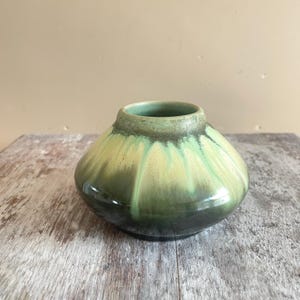 Peut inclure: Un vase en céramique trapu et arrondi doté d'une glaçure brillante qui passe d'un vert forêt foncé à la base à un vert jaunâtre pâle près du col. La surface présente un motif de coulures verticales avec une texture et une profondeur subtiles.