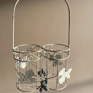 Peut inclure: Porte-bouteilles à vin en métal blanc cassé avec une poignée. Le support comporte deux compartiments et est décoré de feuilles de vigne et de grappes de raisin. Le métal a une finition vieillie.