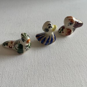 Peut inclure: Trois figurines de canards en céramique peintes à la main. L'un est orné de vert et d'orange, un autre de rayures bleues et blanches, et le troisième de motifs bruns et rouges. Ces canards décoratifs sont probablement destinés à l'exposition.