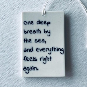 Può includere: Ornamento rettangolare in ceramica bianca con la scritta "one deep breath by the sea, and everything feels right again" in corsivo blu scuro. Un filo bianco è attaccato per appenderlo.