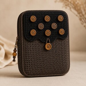 May include: A rectangular, crocheted case in shades of brown and black, adorned with wooden buttons. The top section is black with nine buttons, while the main body is brown. A zipper and a decorative wooden bead tassel complete the design.