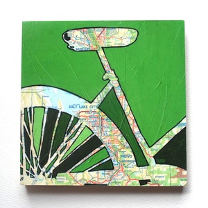 May include: A green and black silhouette of a bicycle is superimposed on a map of Utah. The map shows the cities of Salt Lake City, Provo, and Springville. The bicycle's front wheel is made of green and black spokes.