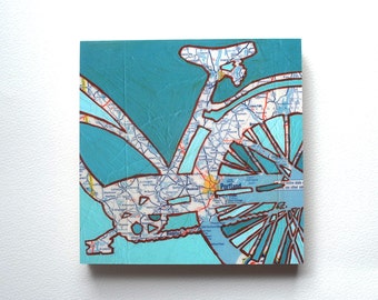 May include: A turquoise blue and brown bicycle silhouette created using a map of Portland, Oregon. The map shows the city's roads and streets. The word "Portland" is visible on the map.