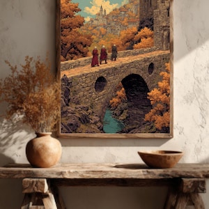 Puede incluir: Una impresión enmarcada representa un puente de piedra con tres figuras que lo cruzan. El puente cruza un río, que conduce a un pueblo situado entre árboles con colores otoñales. La obra de arte está en un marco de madera.
