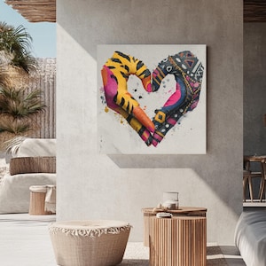 Puede incluir: Una impresión artística en lienzo cuadrada que presenta una forma de corazón formada por dos manos. Las manos están pintadas con colores y patrones vibrantes, incluyendo rayas de tigre amarillas, rosa, naranja y diseños geométricos. La obra de arte se exhibe en una pared de color neutro.