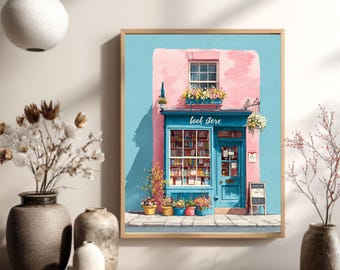 May include: A framed print of a quaint bookstore facade. The building is painted pink and blue, with a blue door and window. The text "book store" is above the door. Colorful flowers in pots line the bottom.