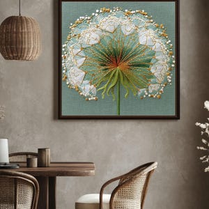 Puede incluir: Una obra de arte enmarcada con un diente de león bordado detallado. La obra presenta un fondo verde claro con un marco marrón. El diente de león está representado con hilo blanco, dorado y verde, con intrincados abalorios en los bordes.