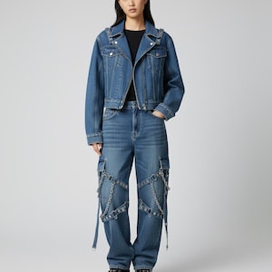 May include: A denim jacket and matching jeans ensemble. The jacket features silver-toned stud detailing on the shoulders and lapels. The jeans have cargo pockets and decorative chain accents. The outfit is completed with black platform shoes.