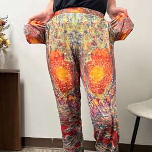 Puede incluir: Pantalones estampados coloridos con un diseño vibrante en tonos naranja, rojo, amarillo y morado. Los pantalones presentan un patrón único y llamativo y un ajuste cómodo y relajado. Una declaración de moda audaz.