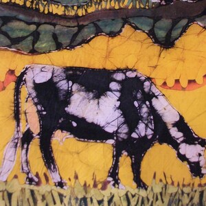 May include: A batik artwork showing a cow grazing. The cow is black and white, set against a yellow background with green and orange accents. The artwork has a textured appearance, with a rural theme.