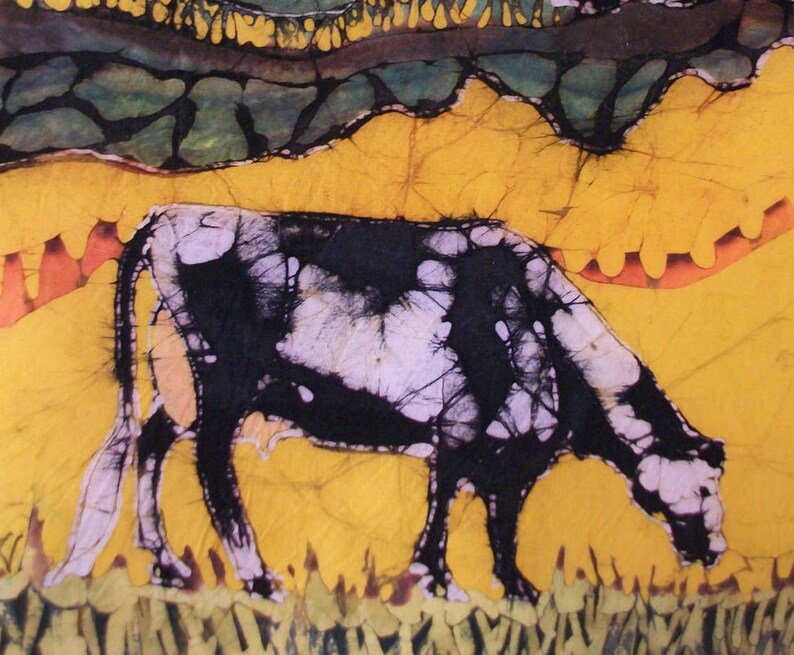 May include: A batik artwork showing a cow grazing. The cow is black and white, set against a yellow background with green and orange accents. The artwork has a textured appearance, with a rural theme.