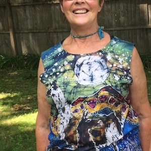 Puede incluir: Una mujer con una camisa sin mangas con un estampado de tie-dye colorido. La camisa tiene un círculo blanco grande en el centro y una variedad de otros colores y diseños. La mujer sonríe y lleva gafas.