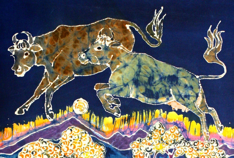Puede incluir: Una pintura batik que representa dos vacas marrones y azules sobre un fondo azul con acentos amarillos, naranjas, morados y blancos. Las vacas est&aacute;n en una pose de salto, con una vaca en primer plano y la otra en el fondo.
