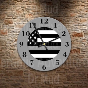 May include: A circular wall clock with a grey face and black numerals from 1 to 12. The center features a black, white, and grey graphic of the American flag with a horizontal grey stripe. The clock has black hour, minute, and second hands.