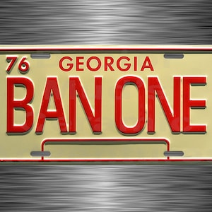 May include: A vintage Georgia license plate with the text "BAN ONE" in red block letters. The plate has a cream-colored background with a red border and the number "76" in the upper left corner. The word "GEORGIA" is above the text.