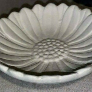 May include: A white, flower-shaped dish with a detailed petal design. The center of the dish has a textured, circular pattern. The dish is made of a solid, opaque material and is likely ceramic or porcelain.