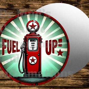 May include: Round metal sign with a vintage gas pump design. The sign features a red gas pump with a star emblem, the words "FUEL UP" in red, and a teal and white sunburst background. The sign is on a wooden background.