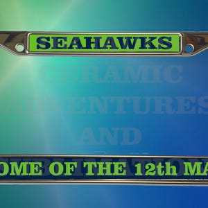 May include: Chrome license plate frame with the text "SEAHAWKS" at the top and "HOME OF THE 12th MAN" at the bottom. The text is in green and blue, with a blue and green gradient background.