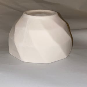 May include: A white, geometric ceramic bowl with a faceted design. The bowl has a wide, hexagonal base and a narrower opening. The surface has a matte finish. This decorative bowl is suitable for home decor.