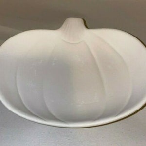 May include: A white ceramic pumpkin-shaped bowl. The bowl has a stem and is designed with vertical ridges, giving it a realistic pumpkin appearance. The bowl is suitable for decorative or functional use.