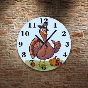 May include: A round wall clock with a light blue face featuring a cartoon turkey wearing a pilgrim hat. The turkey is giving a thumbs up. The clock has black numbers and hands, with a green grass base and pumpkins and apples.