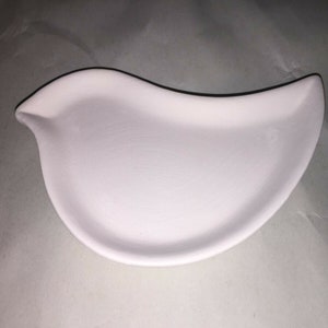 May include: A white ceramic bird-shaped dish. The dish has a smooth, matte finish and a shallow bowl shape. The bird's head is slightly raised, forming a small spout. The dish is designed for serving or display.