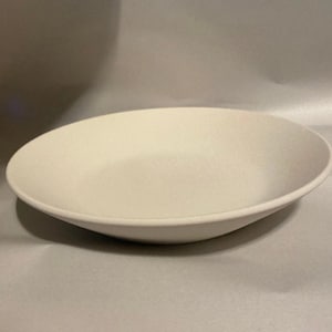 May include: A simple, off-white ceramic bowl with a shallow, rounded design. The bowl has a smooth surface and a slightly raised rim. The neutral color and minimalist style make it suitable for various uses.