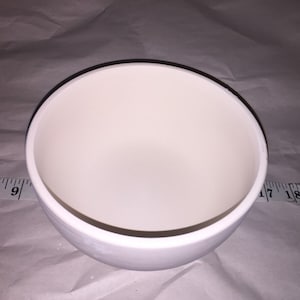 May include: A white ceramic bowl with a rounded shape. The bowl is approximately 7 inches in diameter. The interior of the bowl is smooth and white, and the exterior is also white. The bowl is sitting on a white surface.