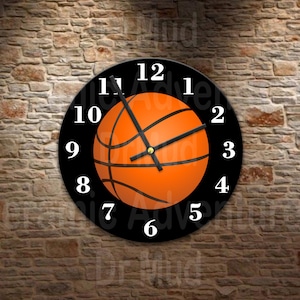 May include: Round black wall clock featuring an orange basketball design. The clock face has white numerals and black hands. The basketball graphic is centered on the clock face. The clock is mounted on a brick wall.