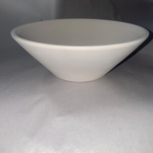 May include: A white, cone-shaped ceramic bowl. The bowl has a wide opening and tapers down to a flat base. The interior and exterior surfaces are smooth and matte. This bowl is suitable for serving food or as a decorative item.
